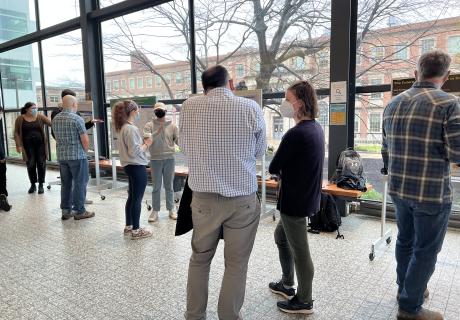 A photo of faculty and students standing and chatting in front of undergraduates' mounted project posters.