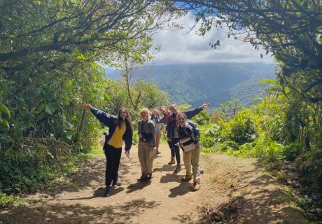 Four students pose facing the camera on a cliffside overlooking a tropical forested view, studying abroad in Central America