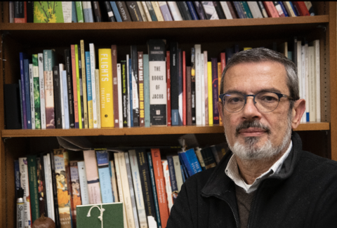 A portrait of Aron Aji in front of a bookshelf