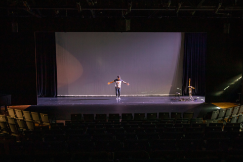 A photo of Lovar Davis Kidd standing solo center stage, head bowed with arms out stretched.