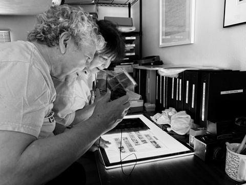 A black and white photo of Johnny Brian and Caroline Pasierb reviewing negatives together.