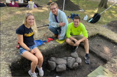 Three anthropology students pose for a photo at a dig site.