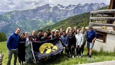 Group of students and faculty holding an Iowa Hawkeyes flag in front of a mountain range