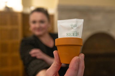 Emily Hurst blurred with focus on her hand holding a miniature terracotta clay pot with miniature seed packet stuffed inside.