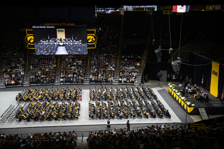 A very wideshot showing the graduates seated in the center with the arena seating and stage in view