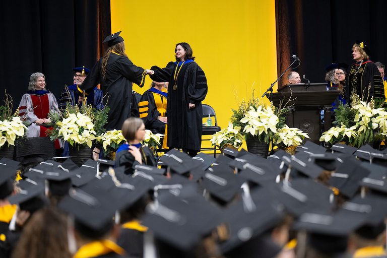 A shot of a student shaking the dean's hand with the crowd in the foreground