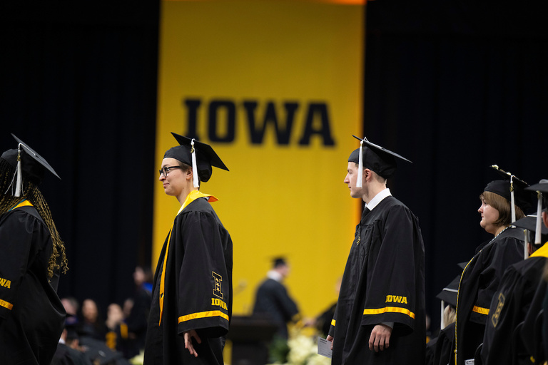 Students crossing the stage with a large iowa banner in the background