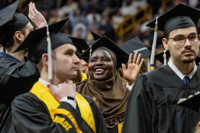 A graduate smiles amongst a crowd as she waves to people in the audience