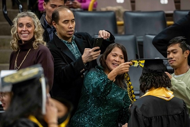 Family members adorn a graduate with a black and gold honorary tassel