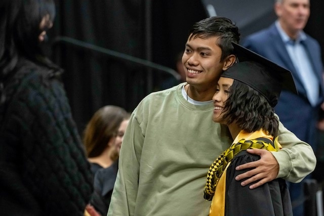 Graduate in cap and gown stands for a photo with a friend or family member