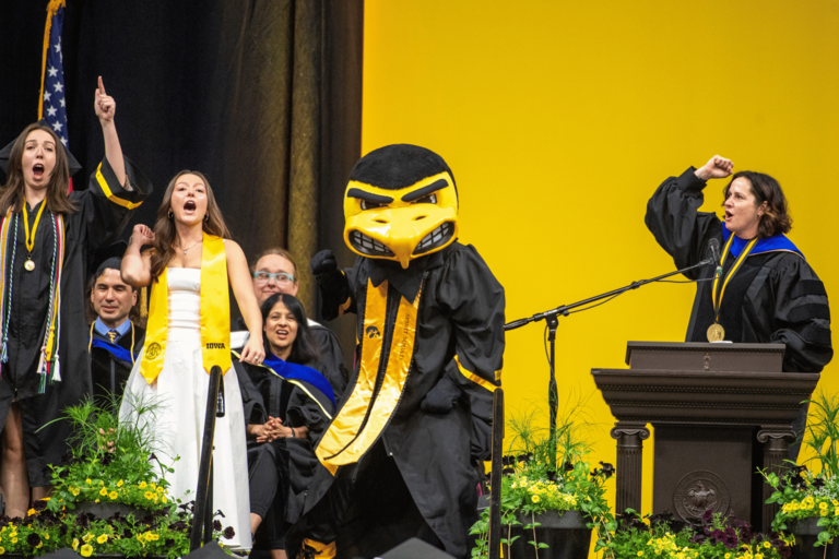 CLAS Dean Sanders stands with the morning Commencement speaker, singer, and Herky the Hawk as each shout out their best "GO HAWKS!"