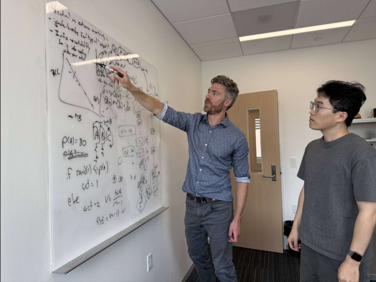 Jeffrey Cockburn helps a student by a whiteboard. 
