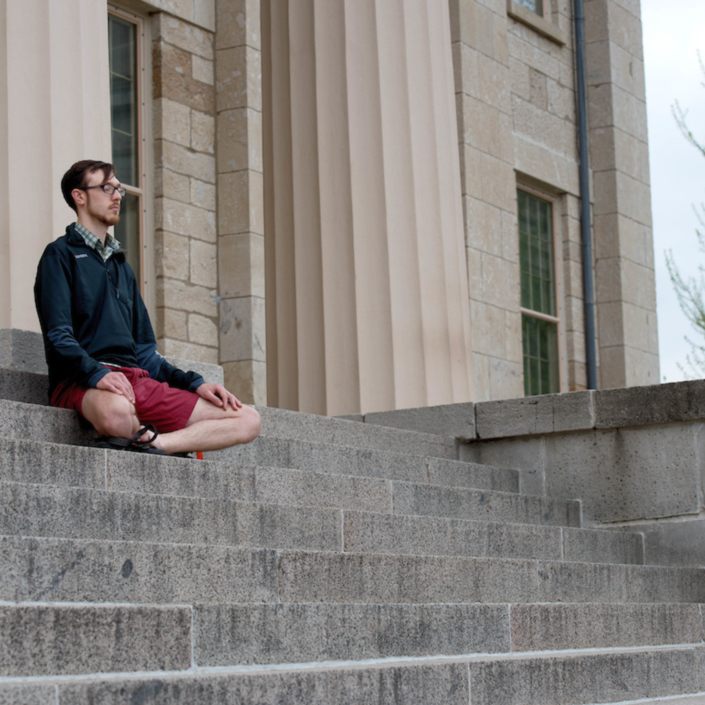 Man meditating on stairs outside of school building on campus