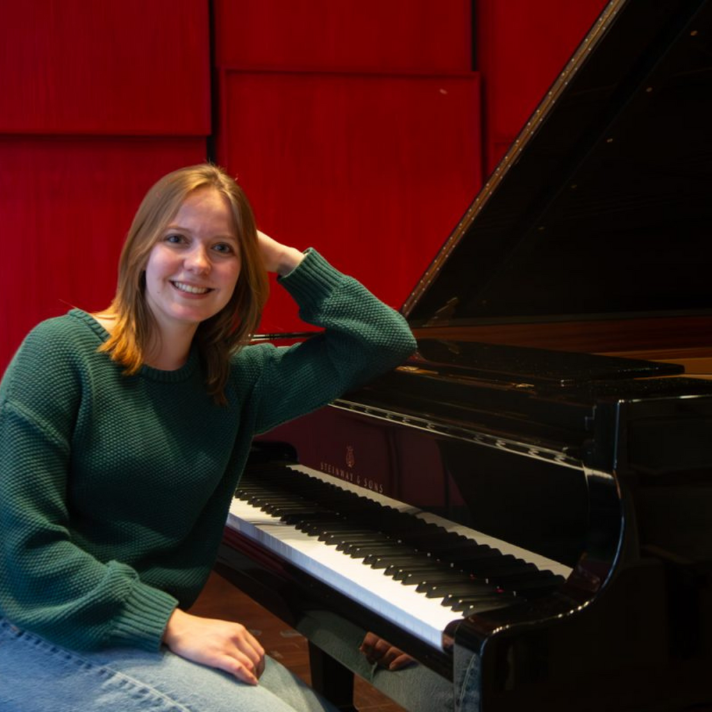 Alison Baldwin, a University of Iowa student double majoring in piano performance and informatics, sits beside a Steinway grand piano in Voxman Music Building.
