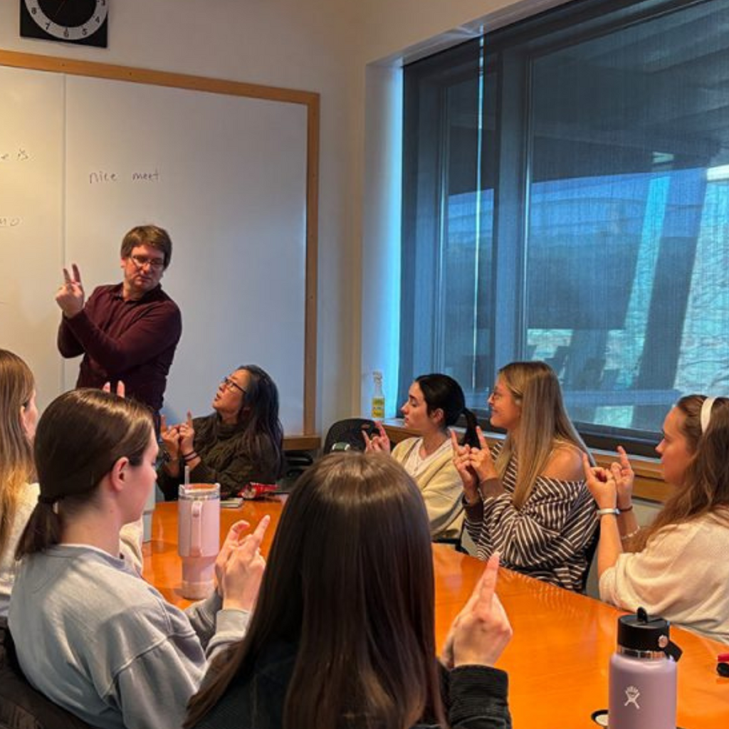 ASL instructor signs in front of a table full of students 