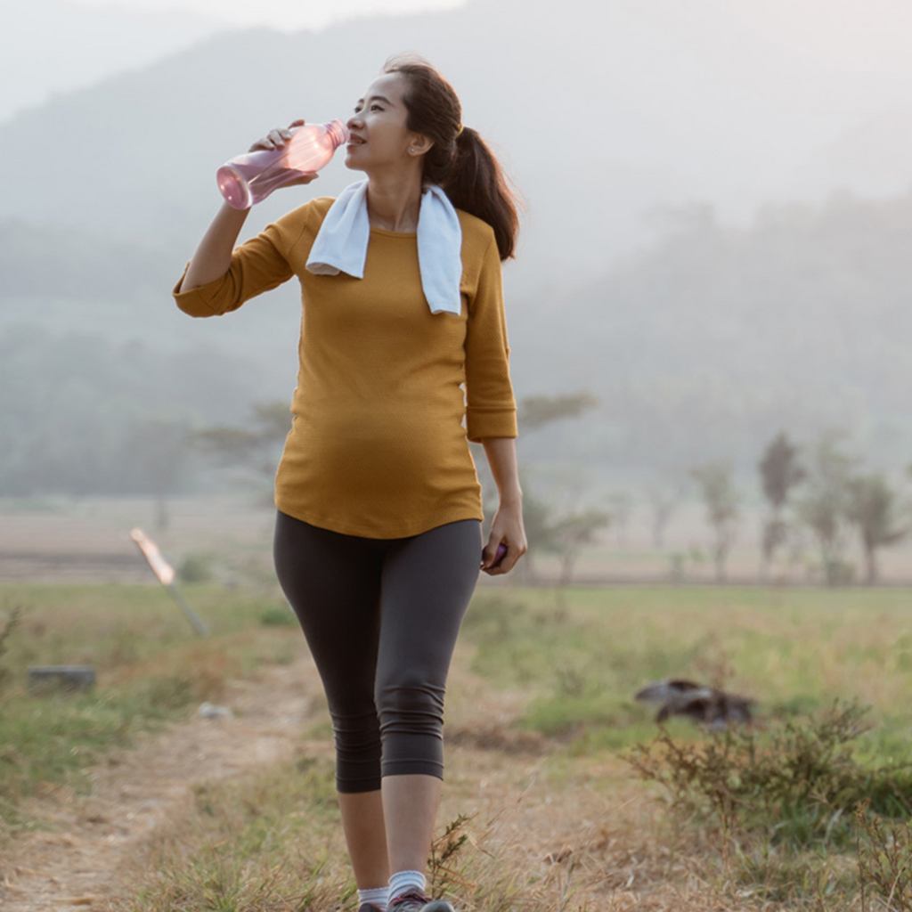 A pregnant woman walks outside drinking water