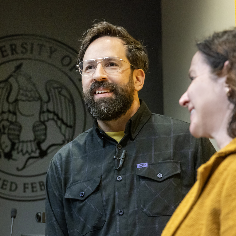 Eric Leiderman smiling towards the audience with Dean Sara Sanders in the foreground