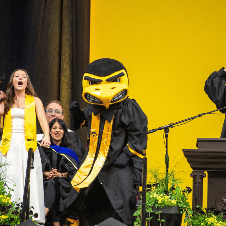 CLAS Dean Sanders stands with the morning Commencement speaker, singer, and Herky the Hawk as each shout out their best "GO HAWKS!"