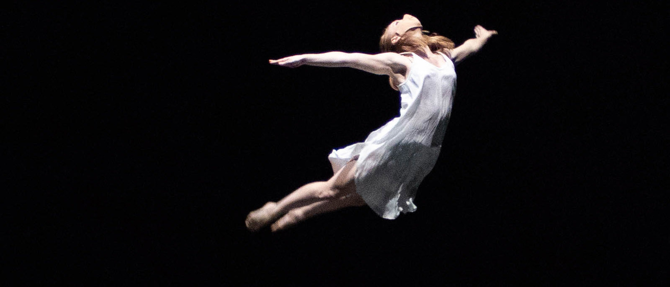 Dancer leaping through the air with arms thrown behind them and legs straight down behind them