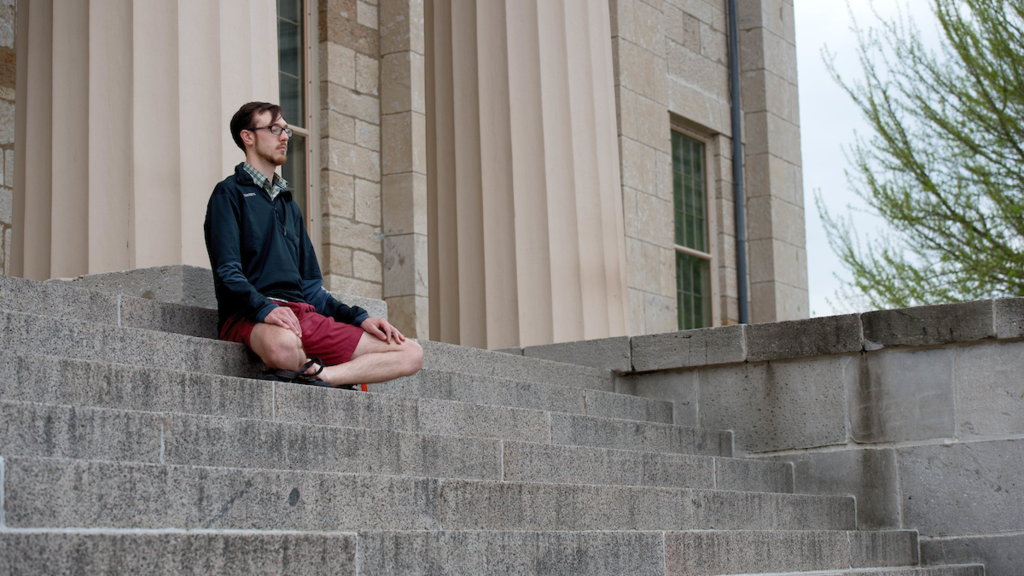 Man meditating on stairs outside of school building on campus