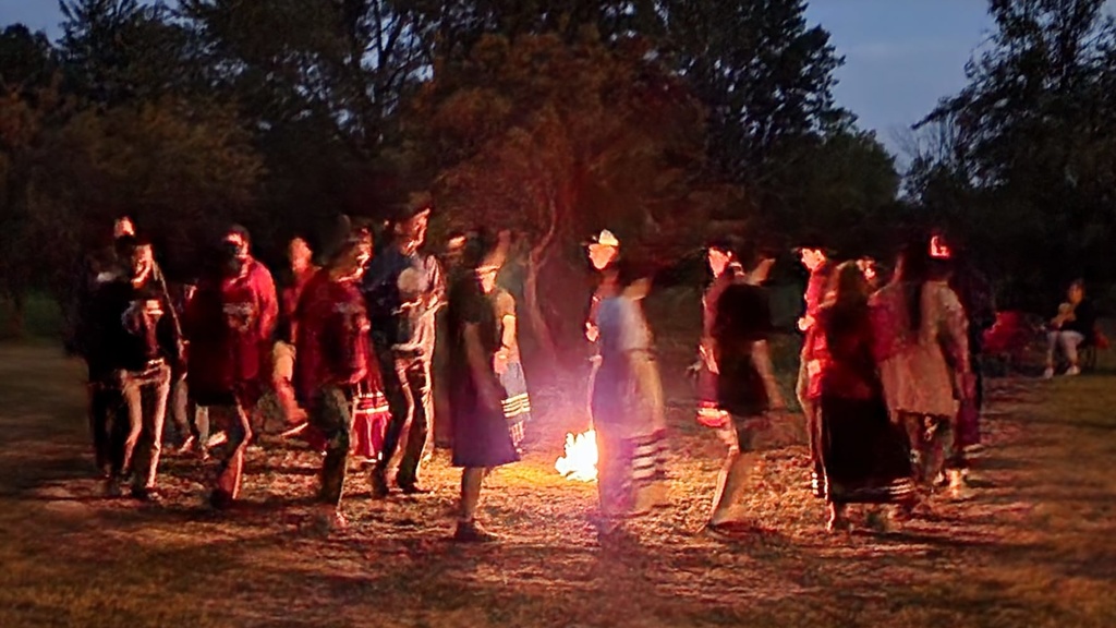 group of people moving in a circle around a fire