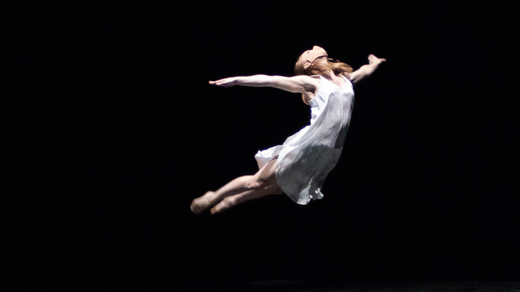 Dancer leaping through the air with arms thrown behind them and legs straight down behind them