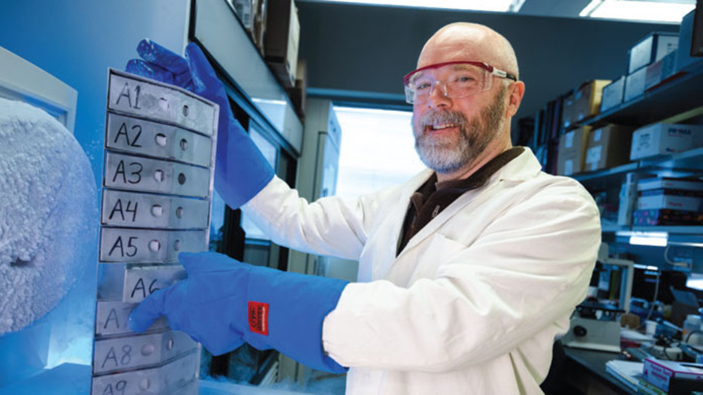 a researcher in lab coat stands in front of a sign with sequenced letters.