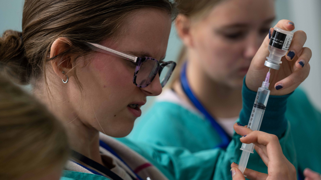 A student in scrubs checks the fill on a syringe