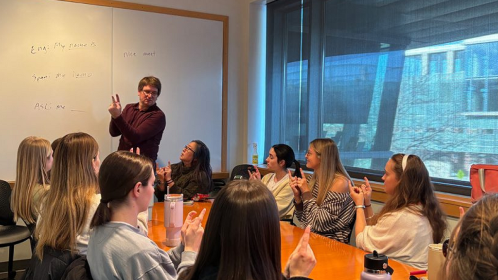 ASL instructor signs in front of a table full of students 