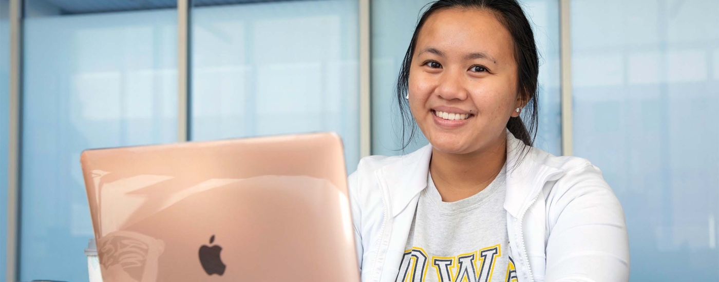 A smiling student working on her laptop at a desk.