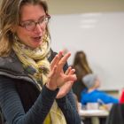 A professor gestures with her hands while addressing the class.